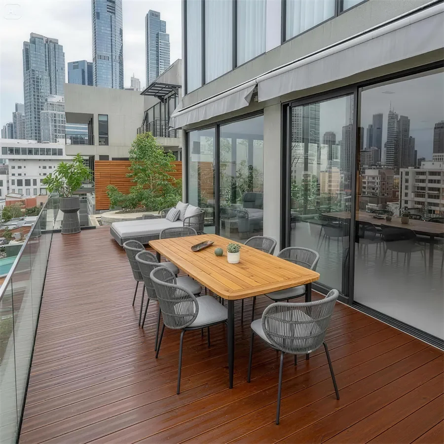 Outdoor patio with a wooden dining table and gray woven chairs, adjacent to a modern apartment building with glass sliding doors, wooden accents, and outdoor seating.