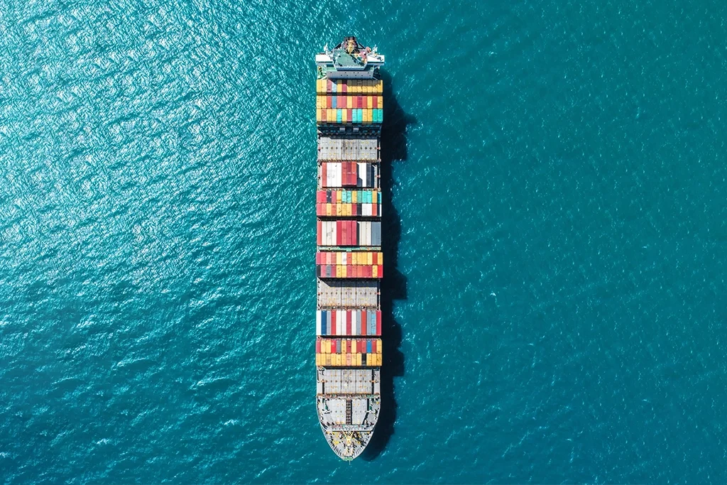 Aerial view of a cargo ship carrying multicolored shipping containers in the ocean.