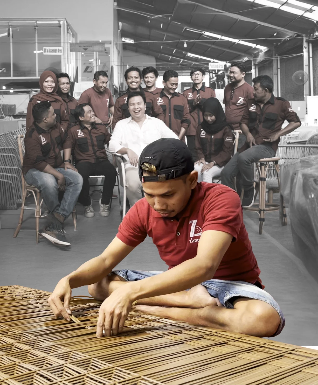 A group of people in uniforms sitting and standing in an assembly area, with a person in a red shirt sitting on the floor in the foreground weaving a bamboo mat.