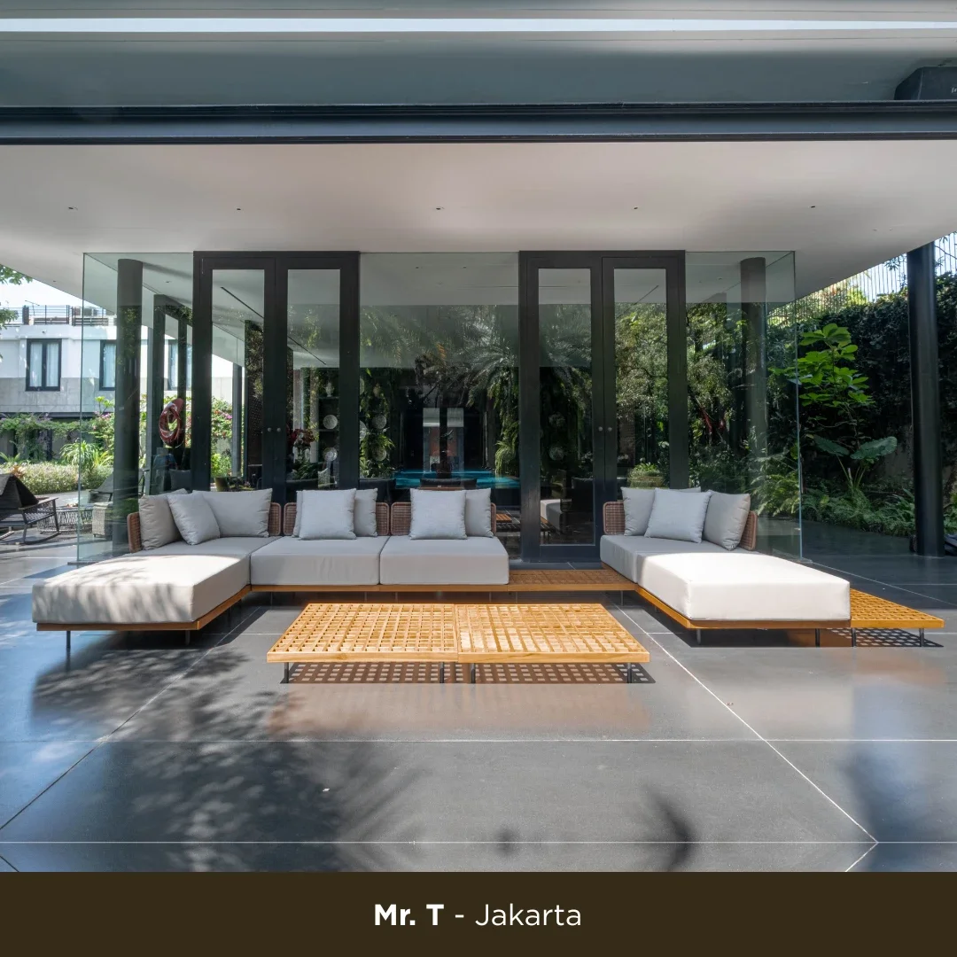 Modern outdoor patio with a large white sectional sofa, wooden lattice coffee tables, and glass walls showing greenery outside.