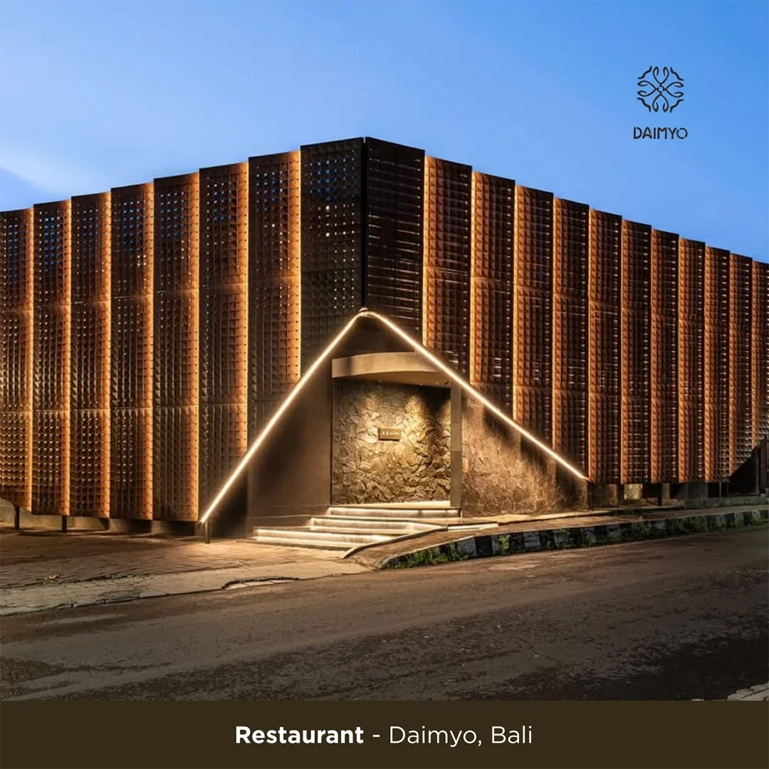 A modern restaurant building in Daimyo, Bali with a unique architectural design featuring warm lighting and a textured stone entrance.