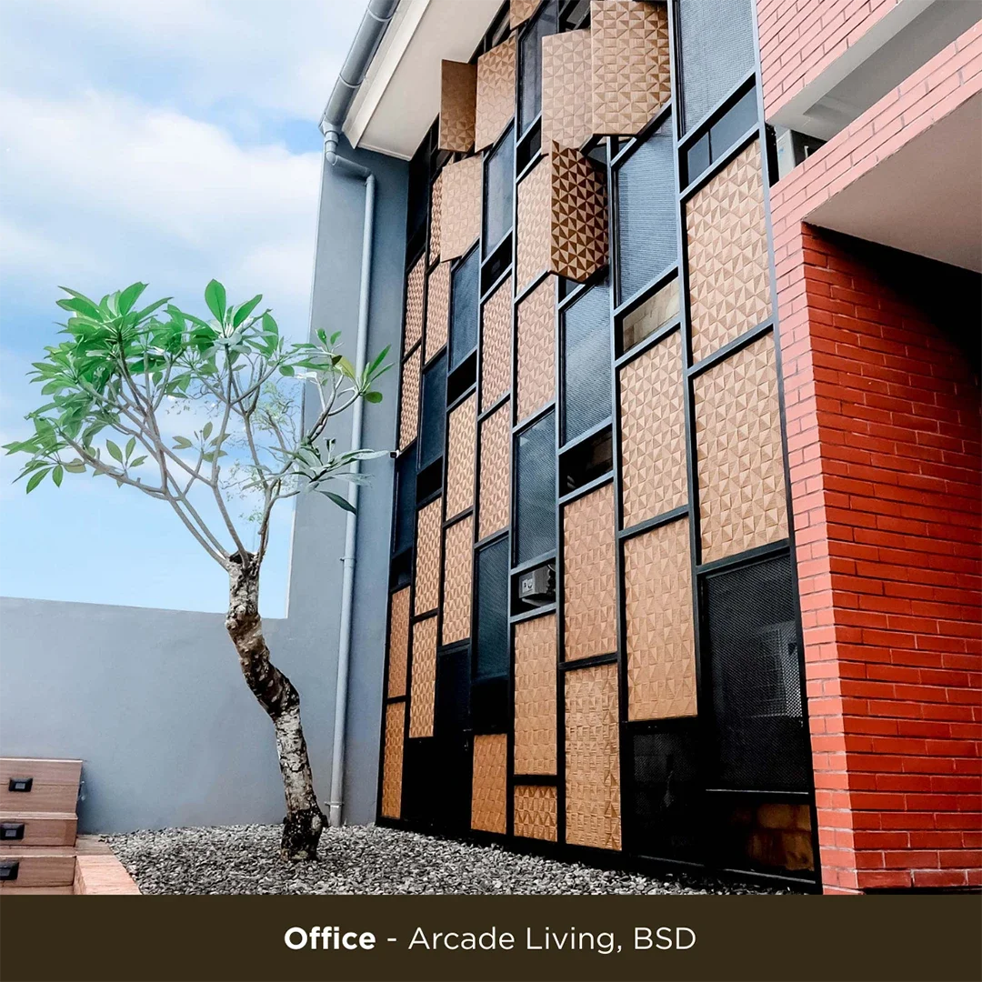 Image of a modern building's exterior with decorative wooden panels, a tree, and a gravel ground. The caption below indicates it is an office at Arcade Living, BSD.