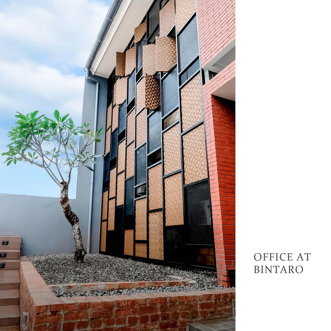 Modern office building with decorative wooden panels on the exterior wall and a small landscaped area with a tree and gravel, labeled 'Office at Bintaro'.
