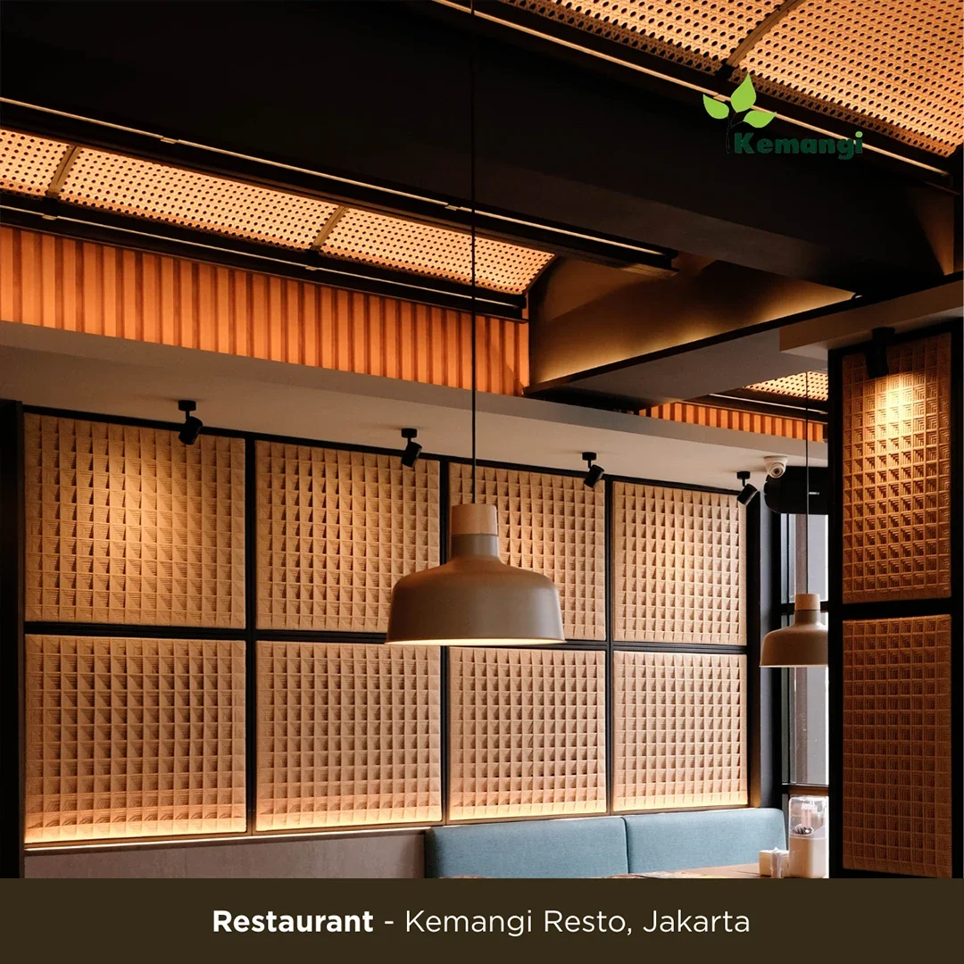 Interior view of Kemangi Resto with wooden acoustic panels on the walls, pendant lights hanging from the ceiling, and a seating area with a blue upholstered bench near a window.