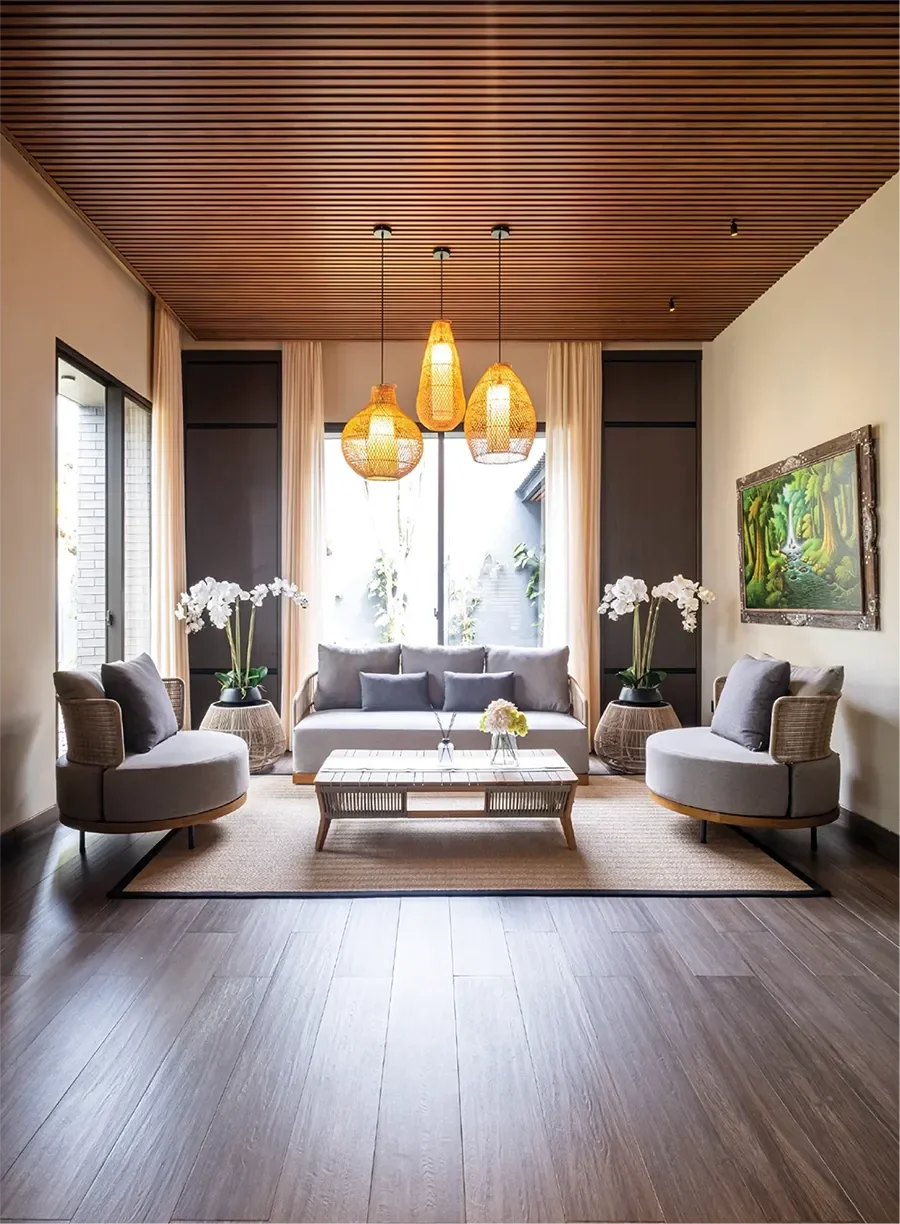 Living room with gray sofa, two round chairs with gray cushions, wooden coffee table, potted orchids, wall art, and hanging wicker lamps