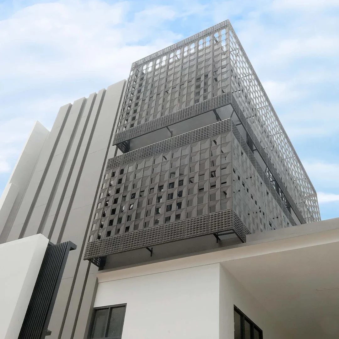 Tall modern building with a dark geometric facade, featuring prominent horizontal and vertical design elements, against a partly cloudy sky.
