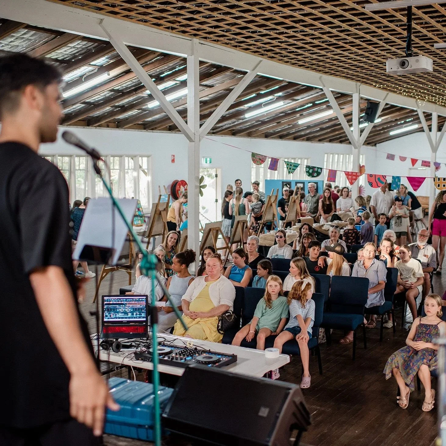 view from stage of a young man at a microphone looking out to a hall of people with bunting