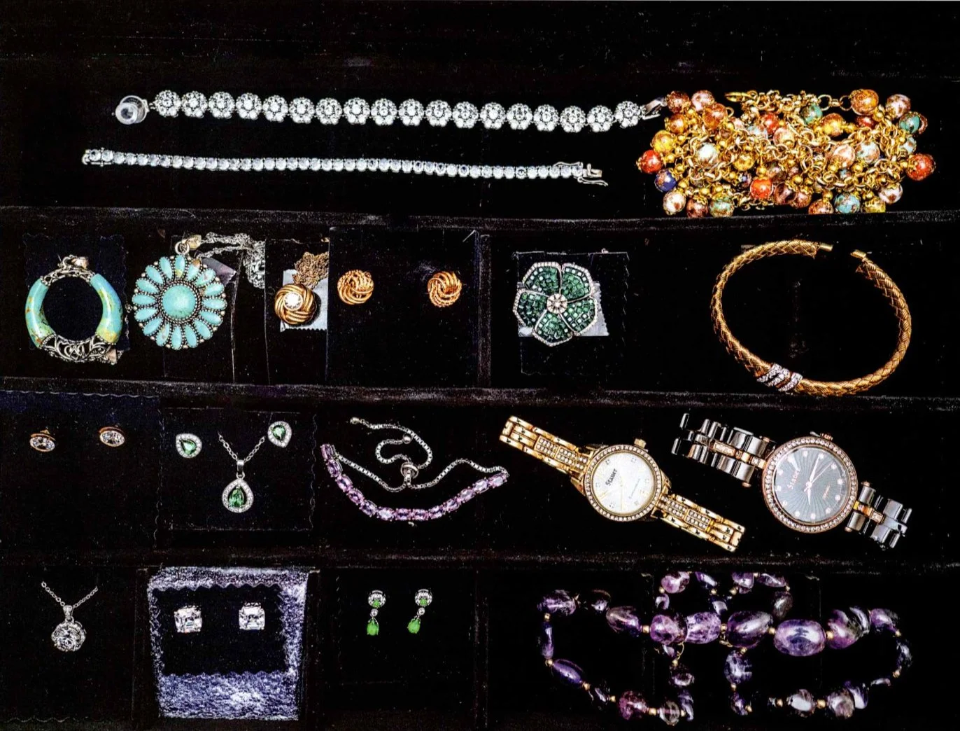 Assorted jewelry including bracelets, necklaces, earrings, and watches displayed in a black jewelry box.