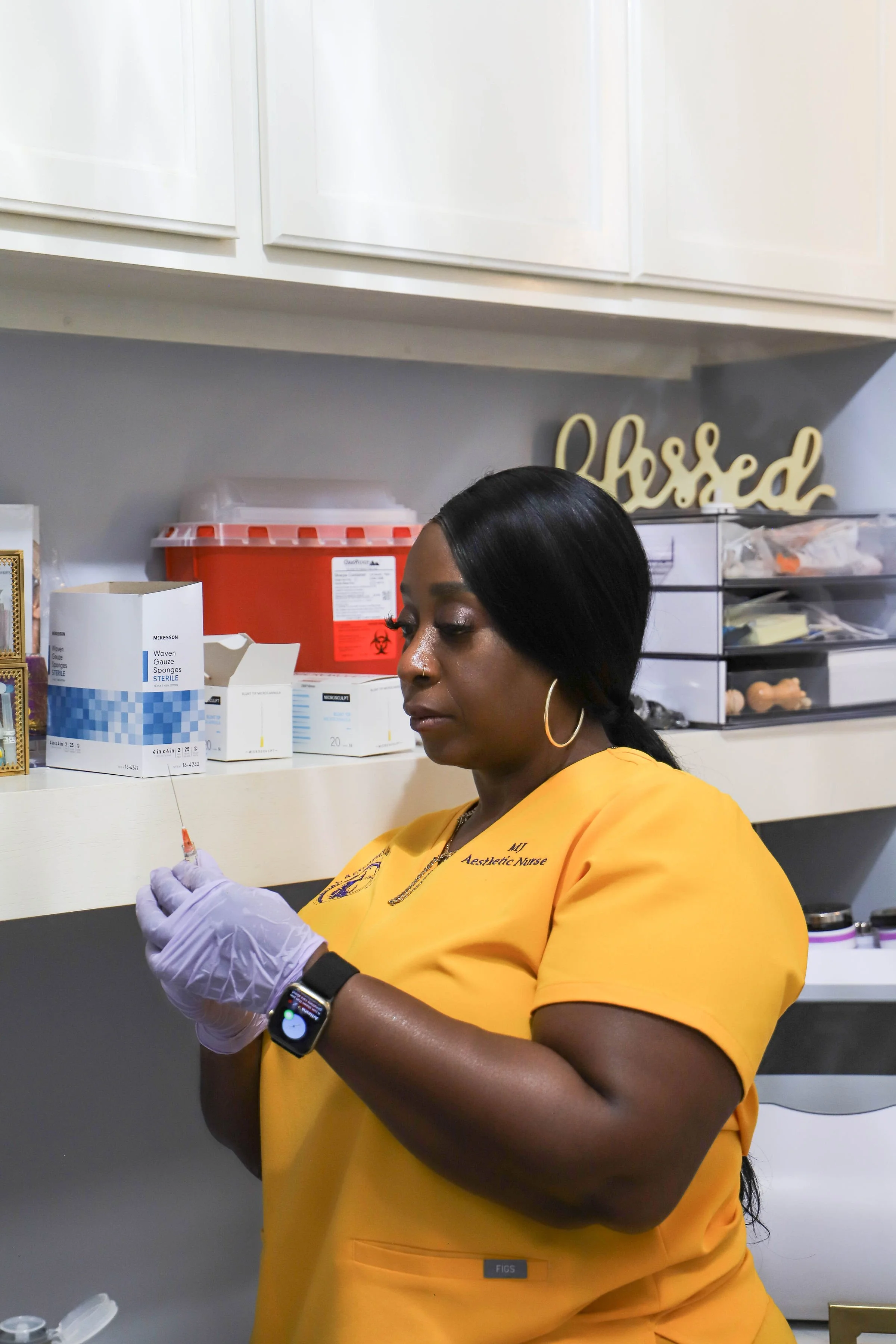 A nurse in yellow scrubs preparing a syringe in a medical supply room.