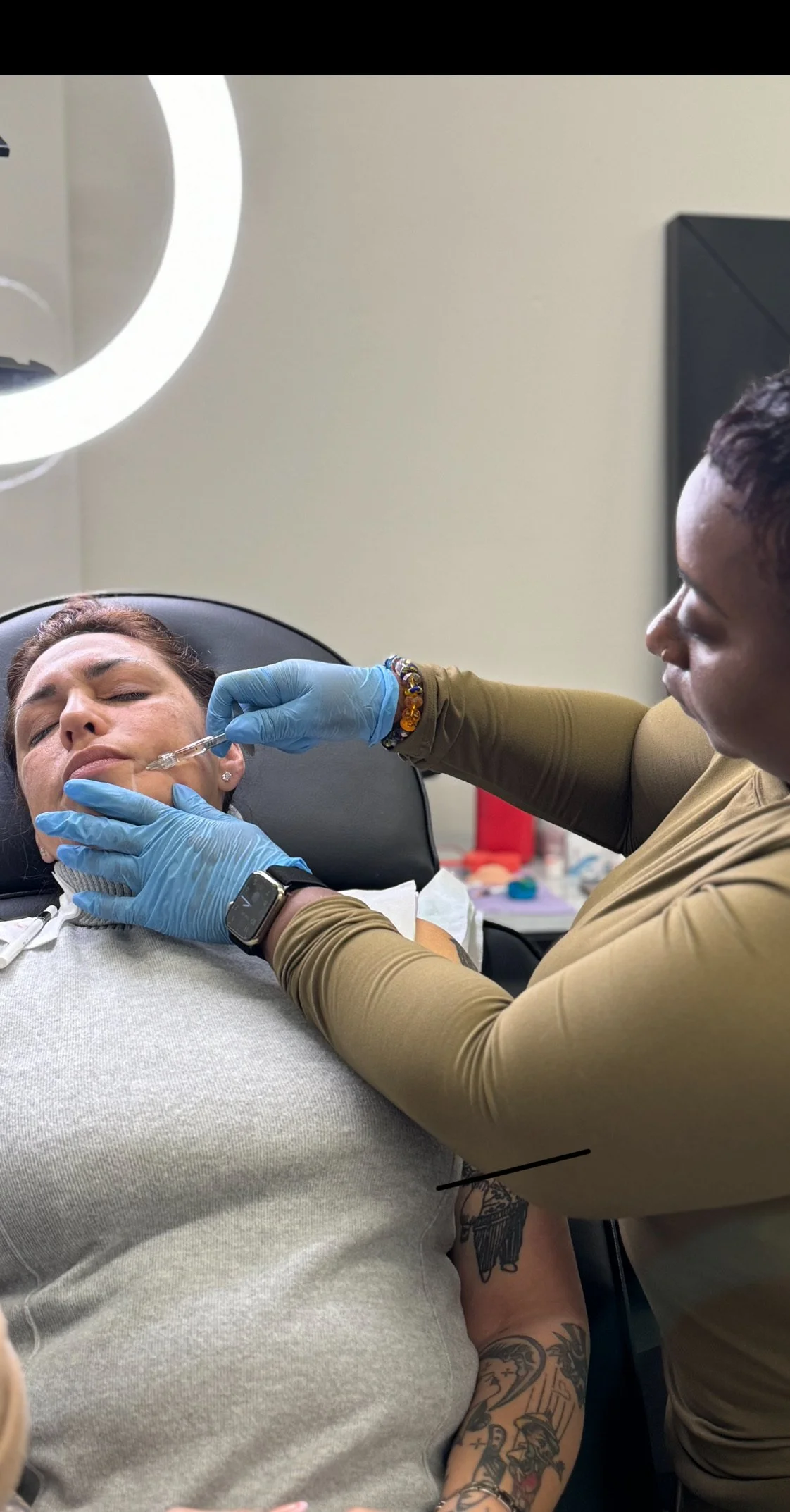 A woman receives a facial injection from a healthcare professional wearing blue gloves in a clinical setting.