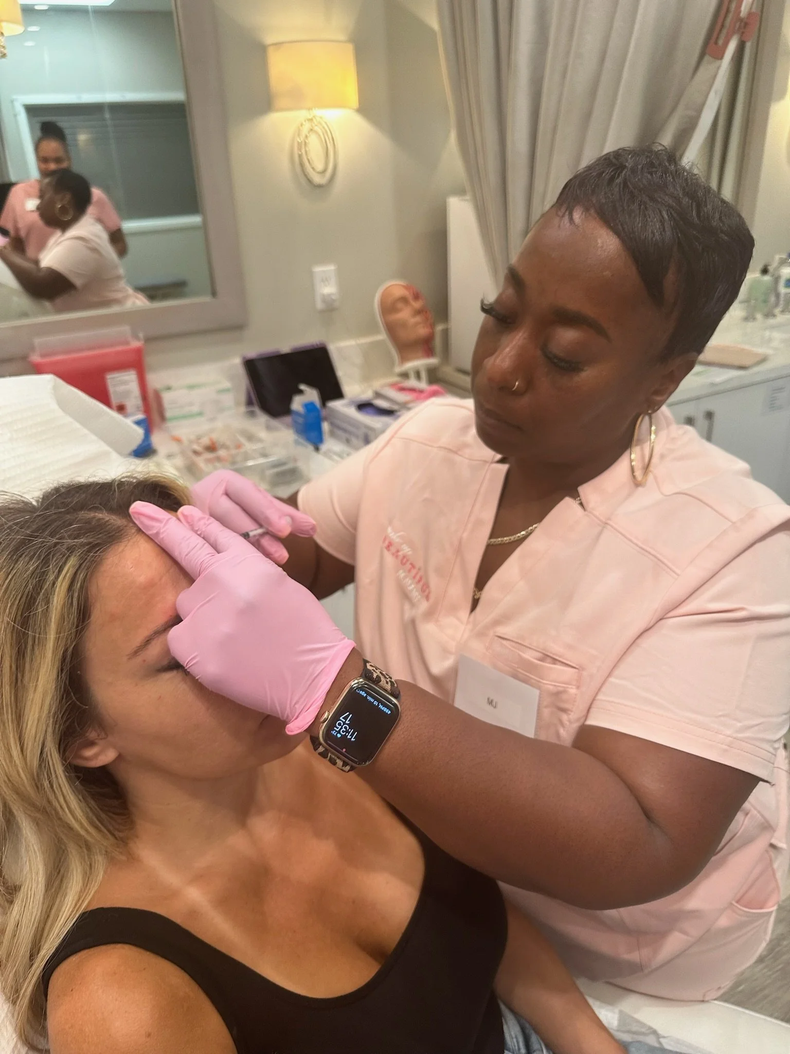 A healthcare professional administering a Botox injection to a woman's forehead in a clinical setting, with medical supplies and a mirror in the background.