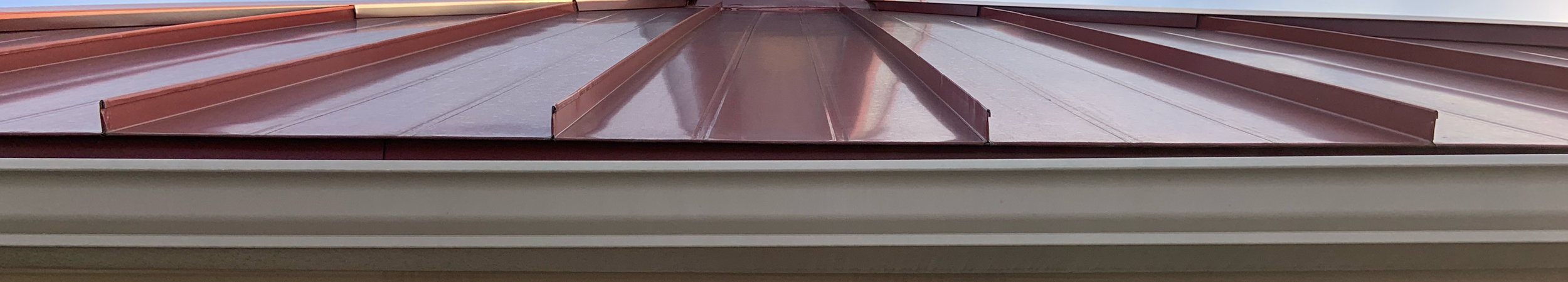 Close-up of red standing seam metal roof panels showing raised seams above the roof edge.
