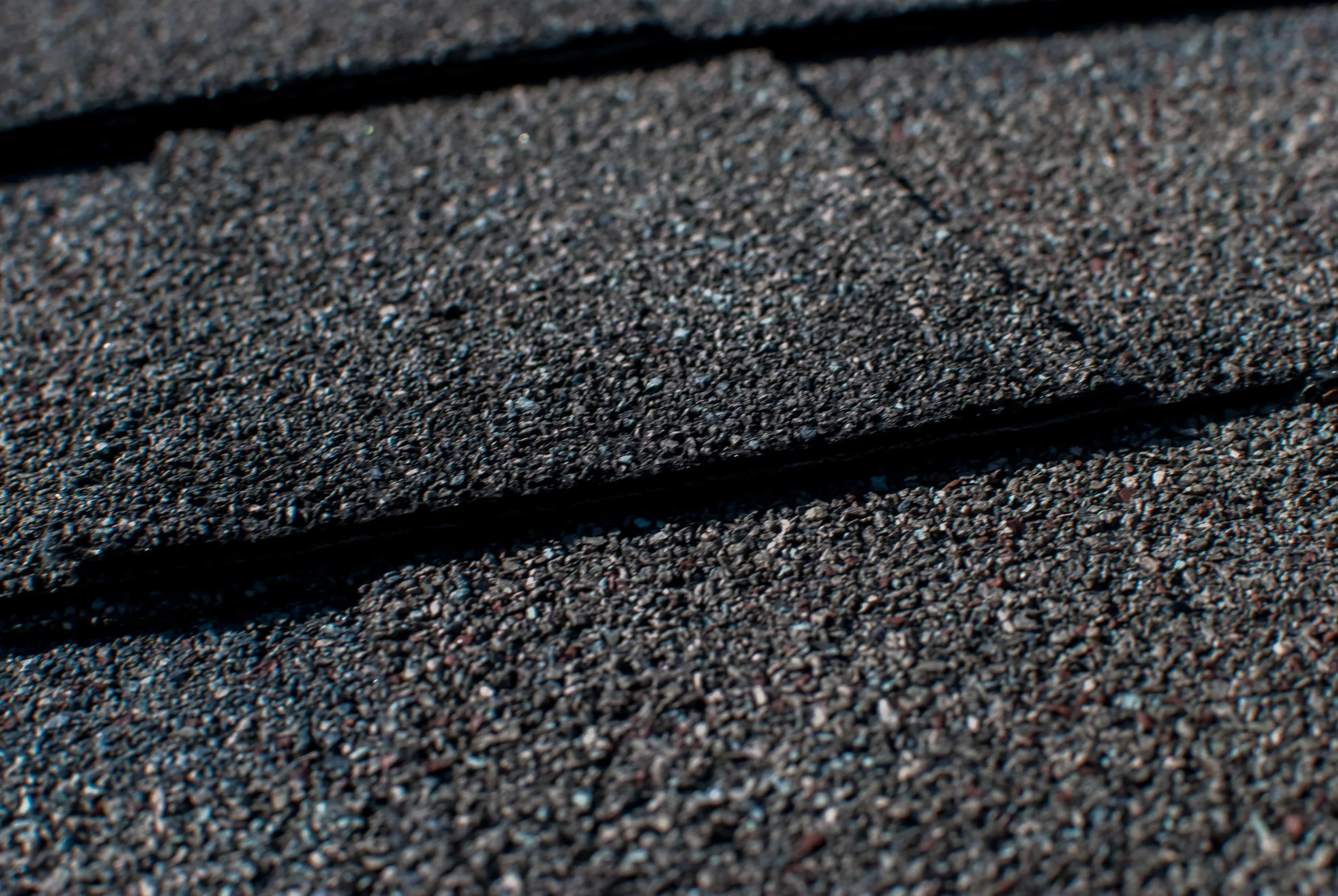 Close-up of dark asphalt roof shingles showing textured granules and overlapping edges.