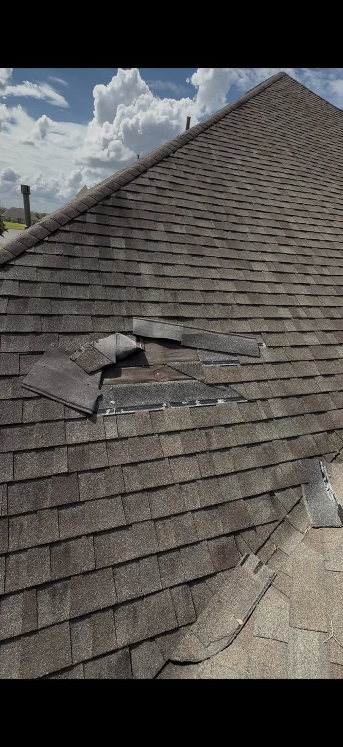 Wind-damaged asphalt shingles with missing and lifted sections before roof repair by Apex Roofing Solutions.