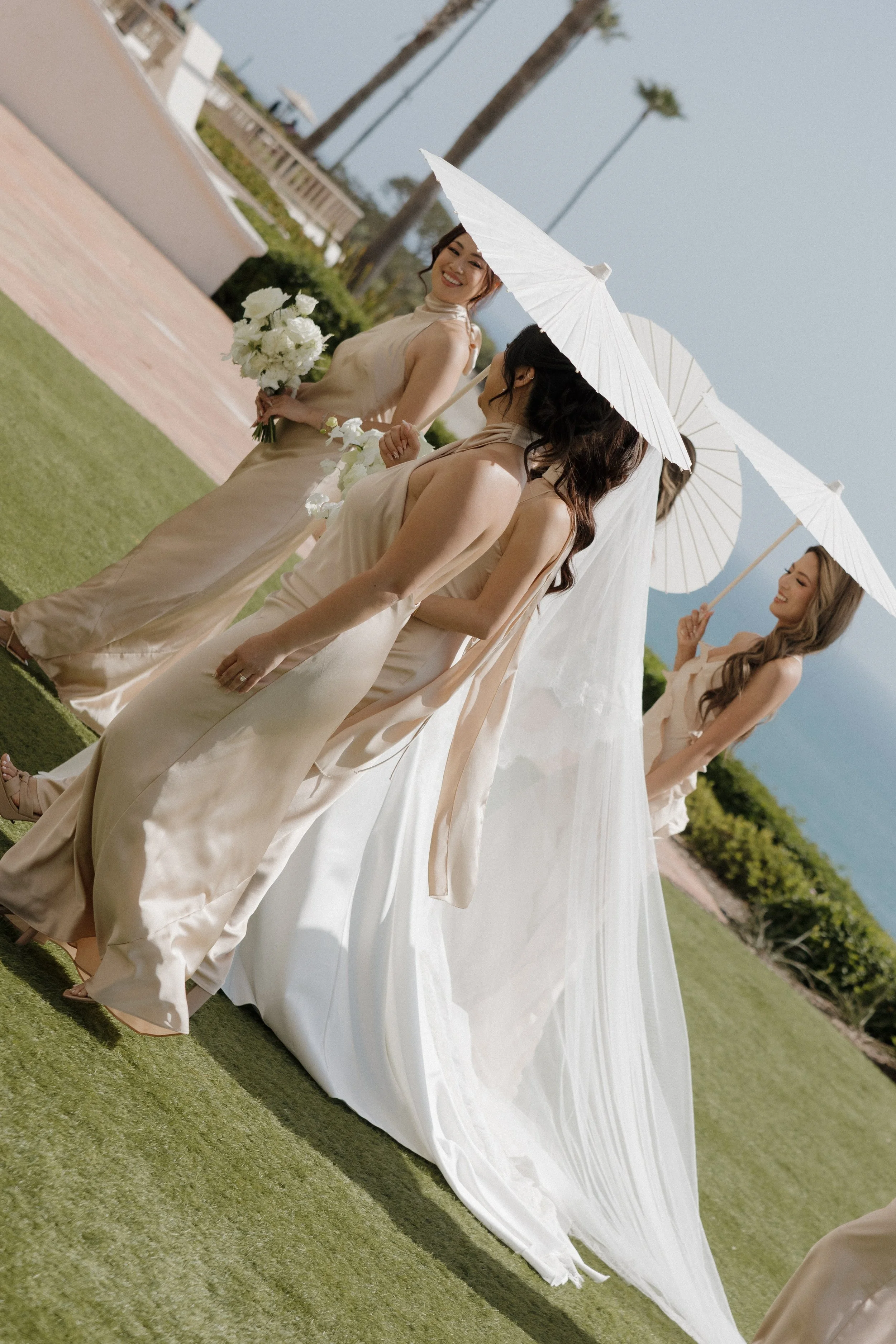 Bridesmaids escorting the bride with a parasol across the lawn, Ritz-Carlton Laguna Niguel