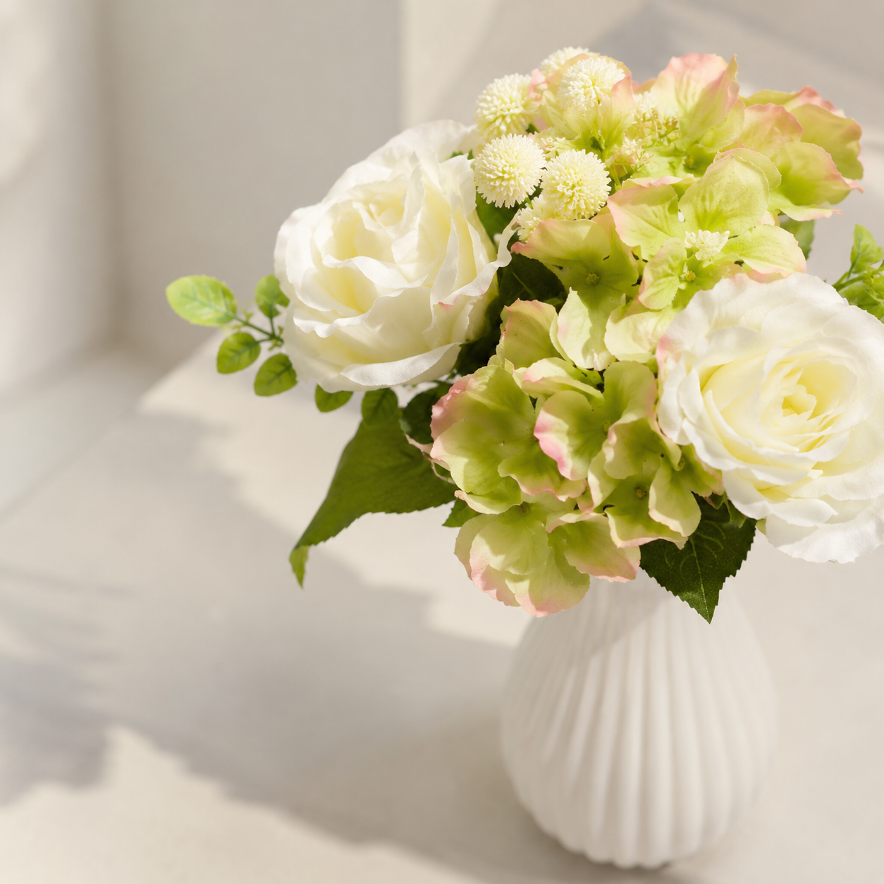 Artificial white rose and green hydrangea bouquet in ribbed vase