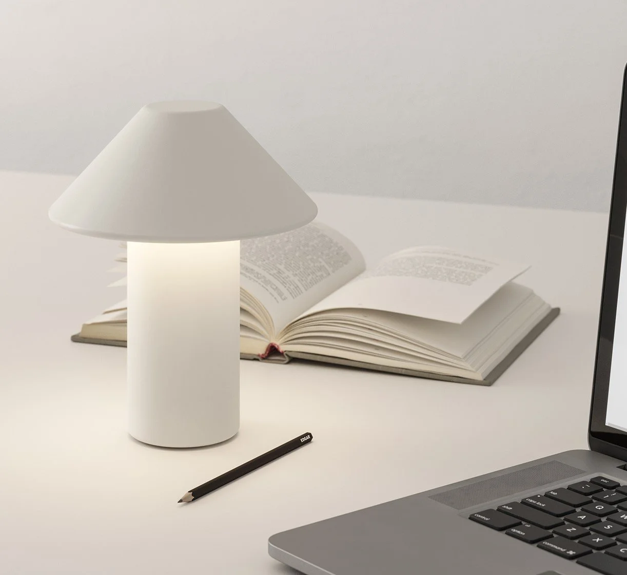 A white desk lamp, an open book, a black pencil, and part of a laptop on a white desk.