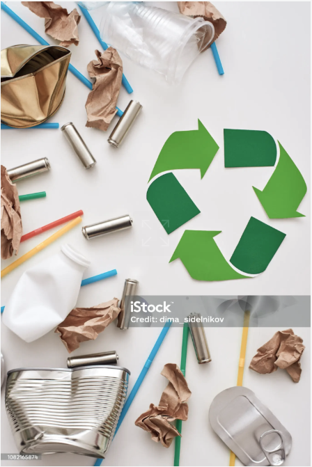 Recycling symbol made of green paper with scattered empty aluminum cans, paper, and straws on a white surface.