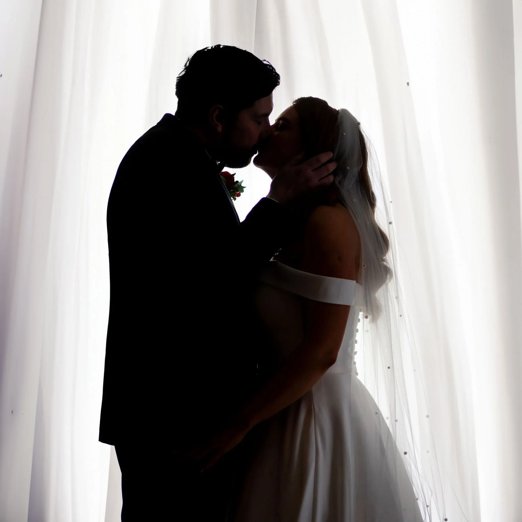 Silhouette of bride and groom kissing by a window