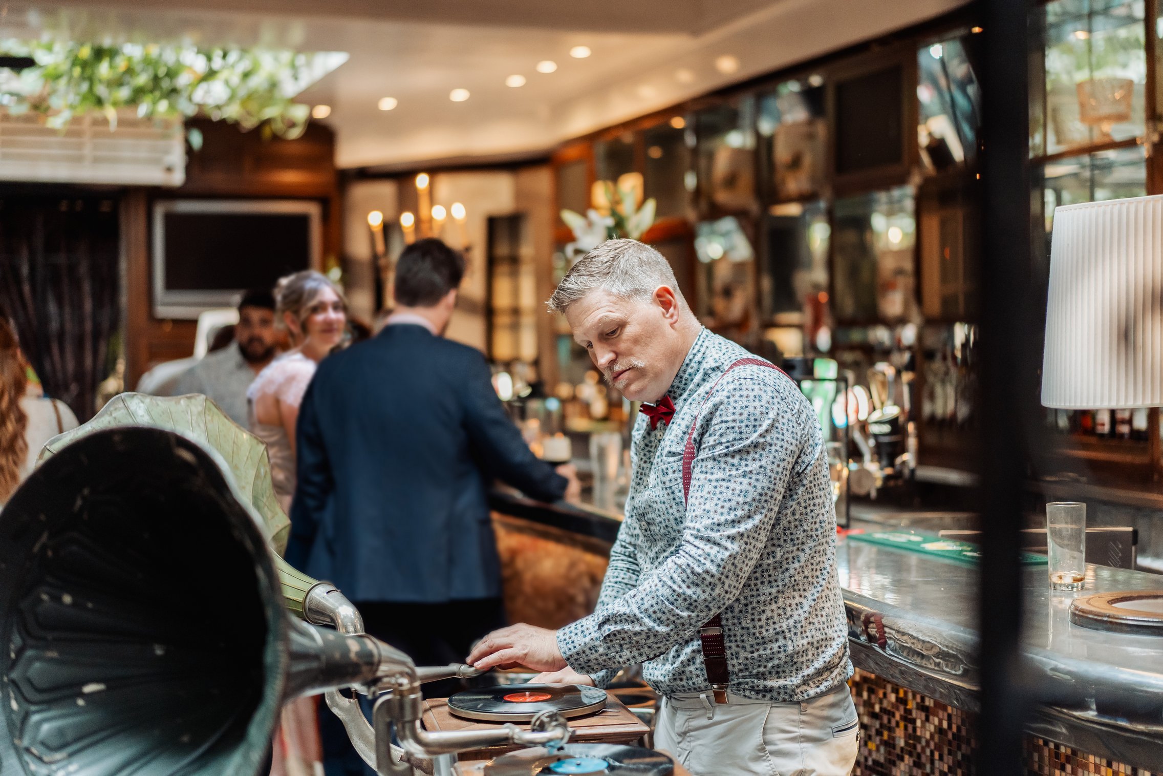 Trevor playing music on a vintage gramophone at a wedding bar with guests listening.