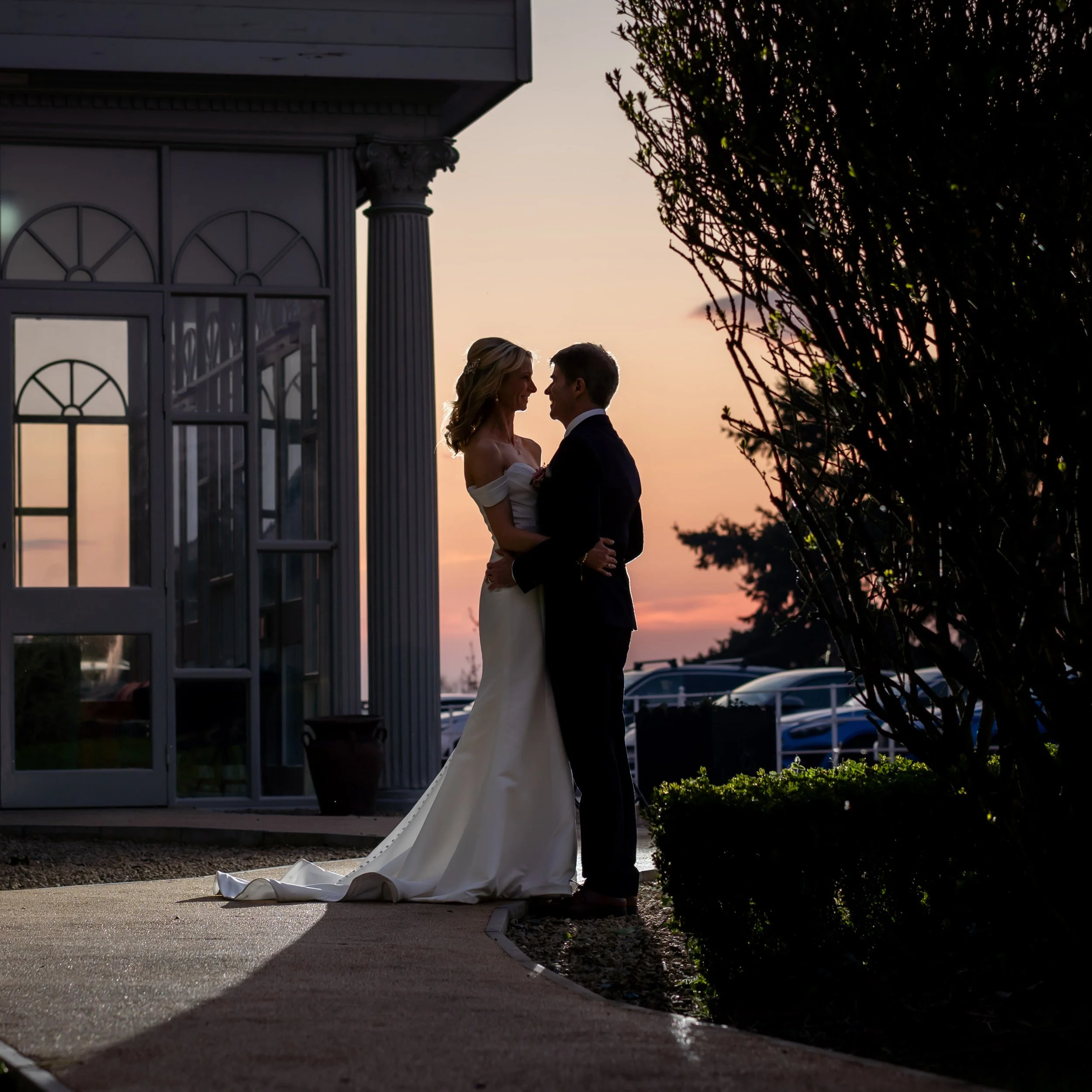 Silhouette of a bride and groom standing together at sunset, with the glowing sky in shades of orange and pink behind them, taken from the grounds of Killashee House Hotel in Naas.