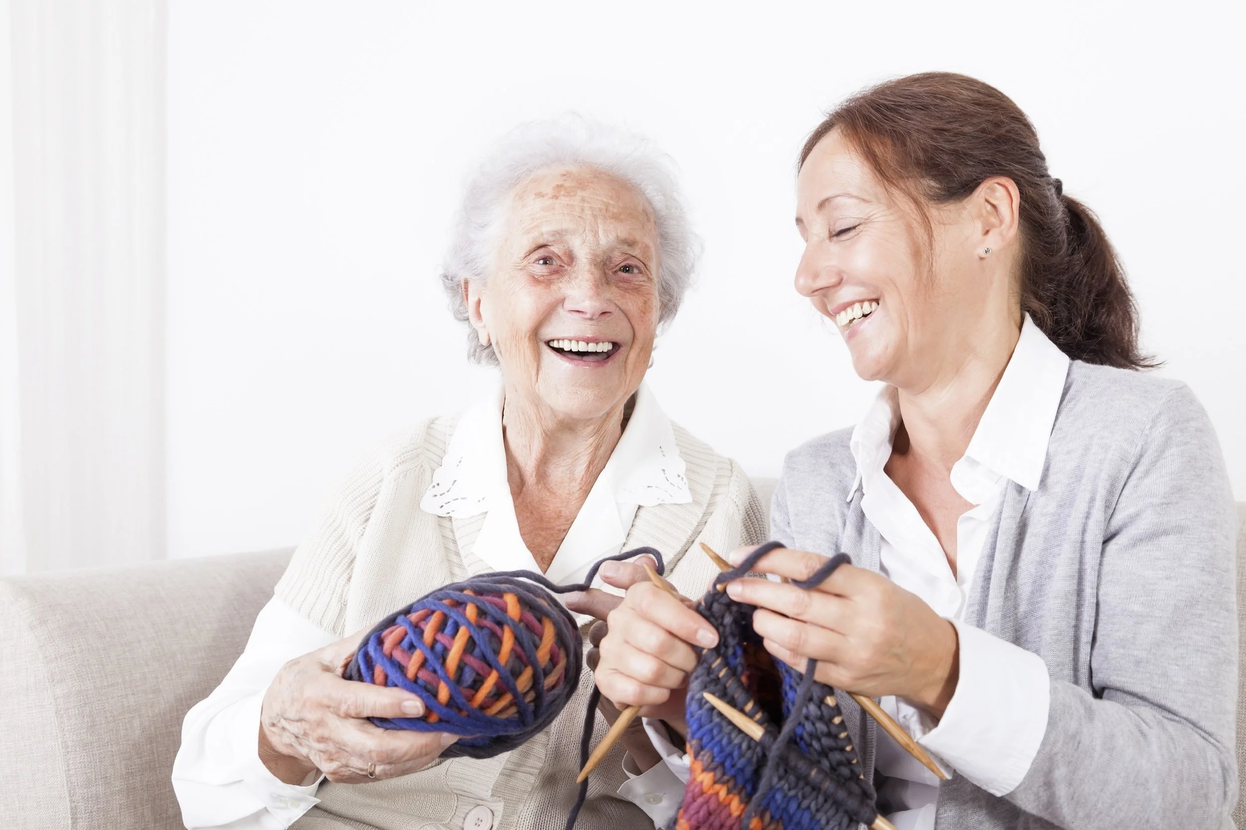 Symbolbild 24-Stunden-Betreuung: Seniorin und Frau haben Spaß beim gemeinsamen Handarbeiten.