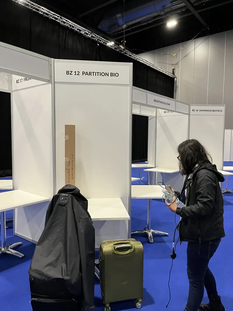 Empty PartitionBio Breakthrough Zone stand BZ12 at ELRIG Drug Discovery 2025 before setup, with a team member and luggage arriving
