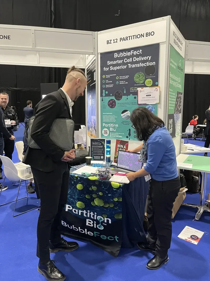 PartitionBio team member demonstrating BubbleFect to a visitor at the ELRIG Breakthrough Zone stand, showing data on a laptop