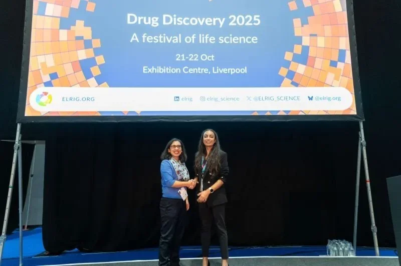 shaking hands on stage in front of the ELRIG Drug Discovery 2025 screen at the Exhibition Centre Liverpool