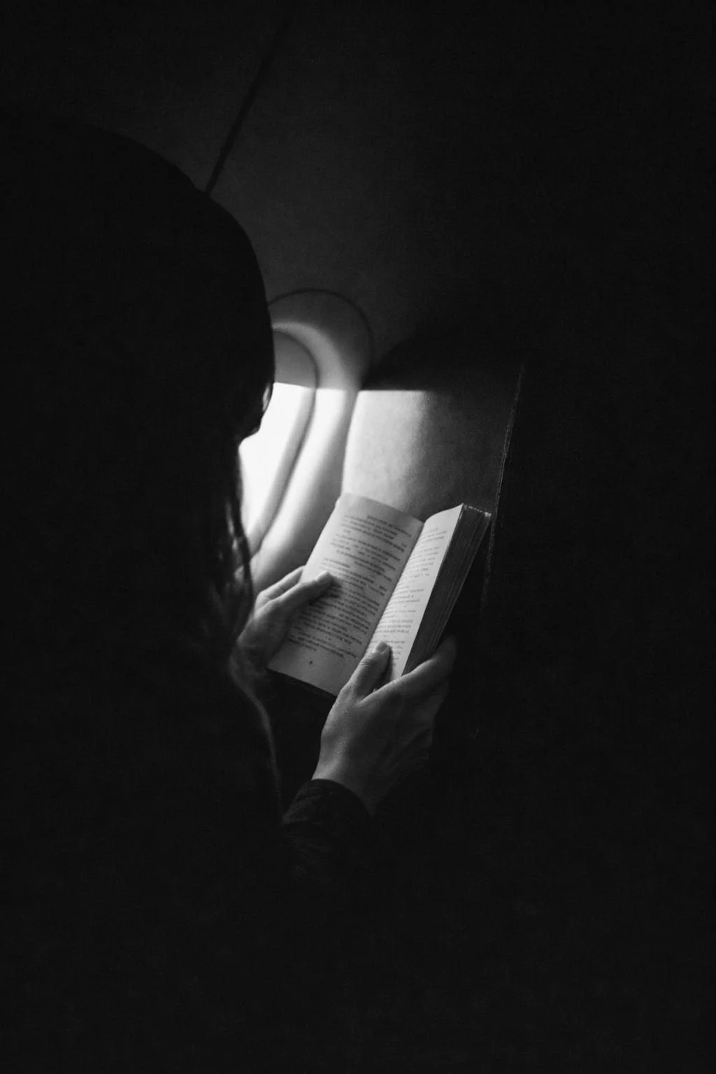 Mano femenina sujetando un libro en papel junto a la ventanilla de un avión, lectura reflexiva en blanco y negro sobre pensamiento crítico y cultura digital.