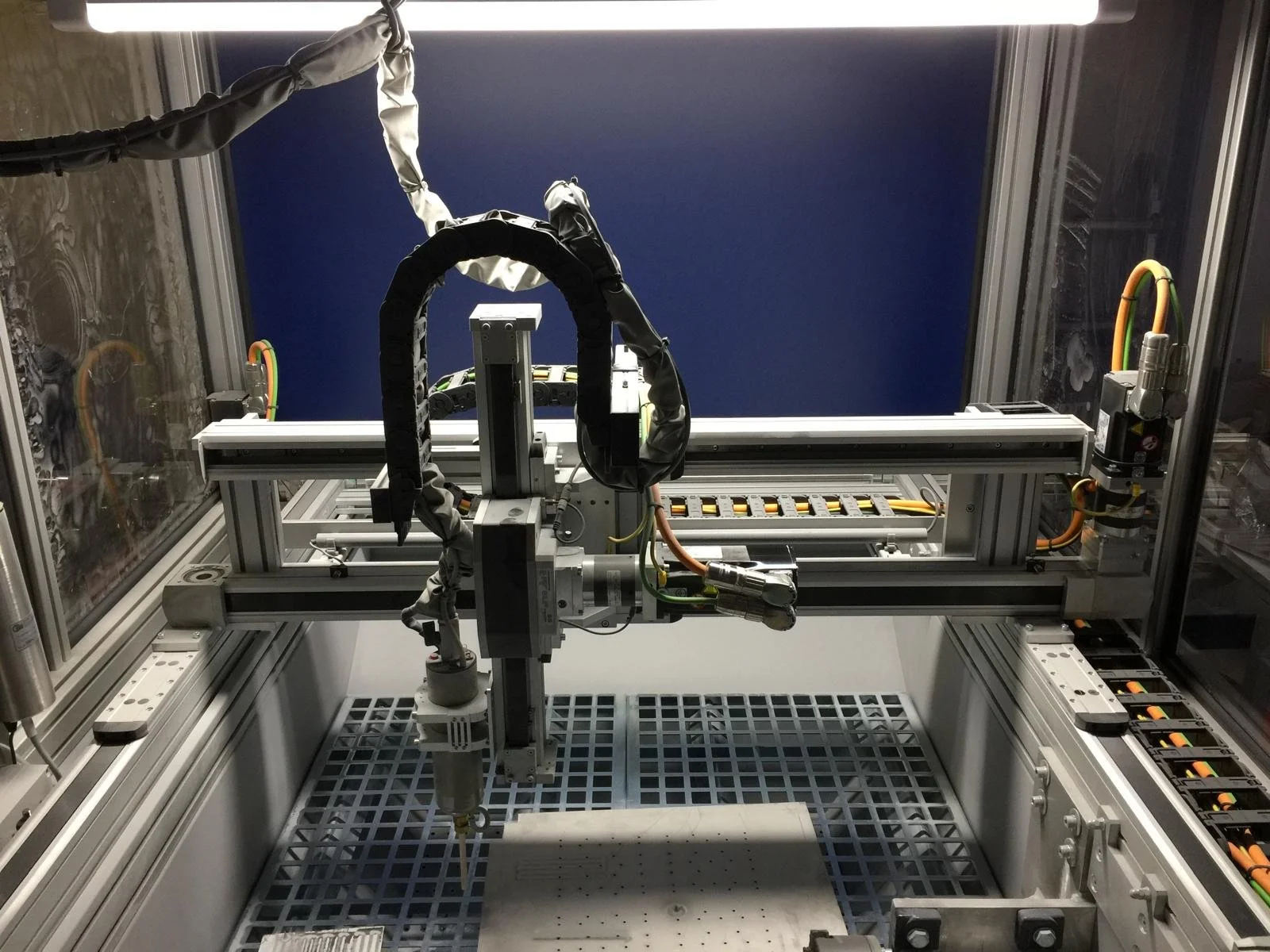 Industrial robotic arm inside a metal frame with electronic components and cables.