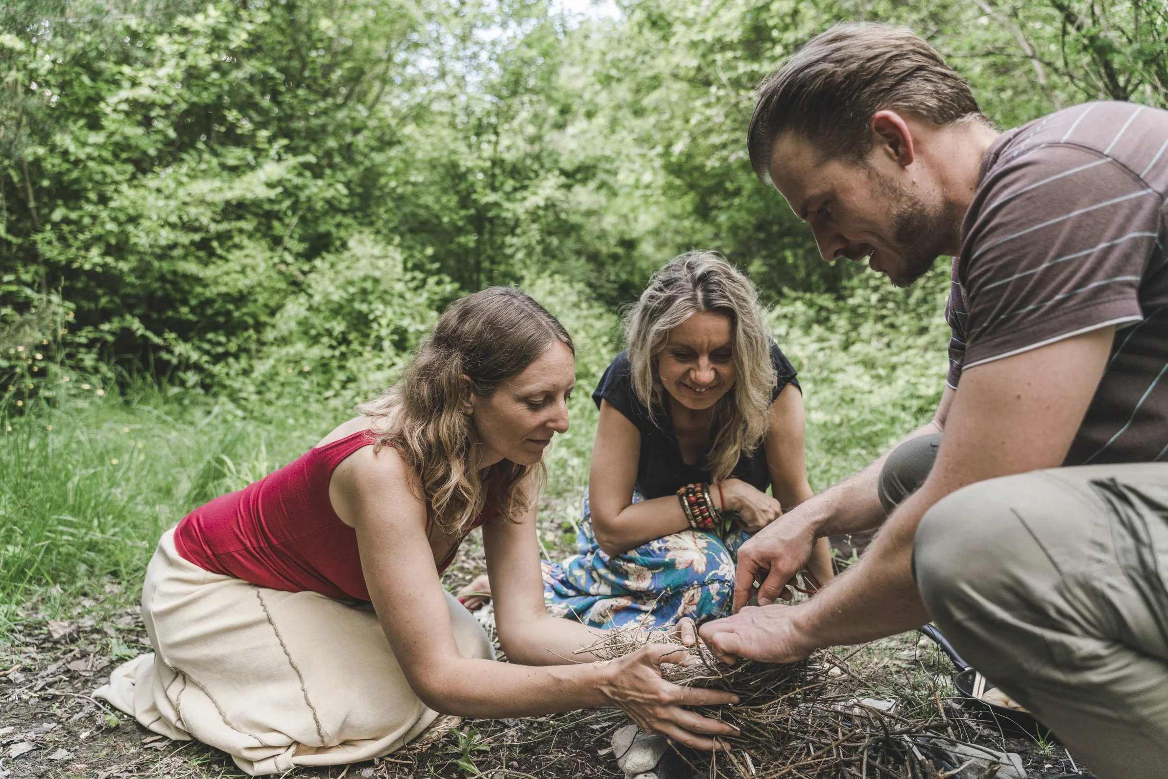 Drei Menschen, die im Wald ein Feuer entfachen wollen. Sie halten das Zundernest.