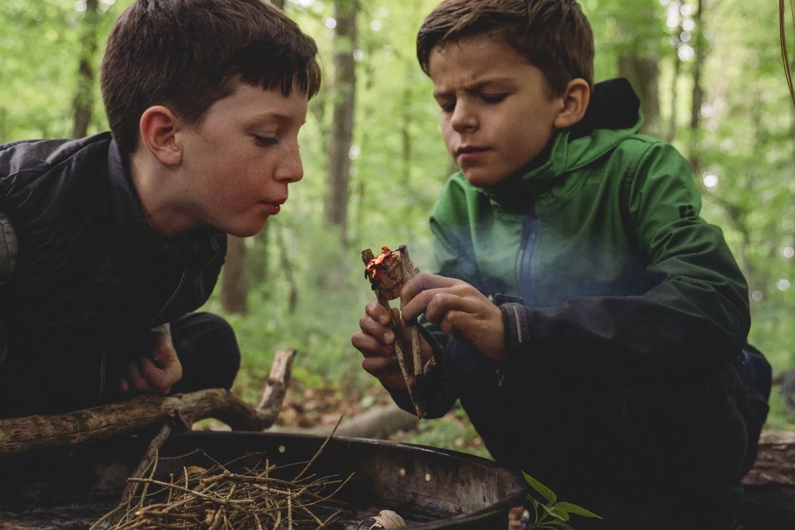 Zwei Jungen im Wald beim gemeinsamen Betrachten eines kleinen Lagerfeuers.