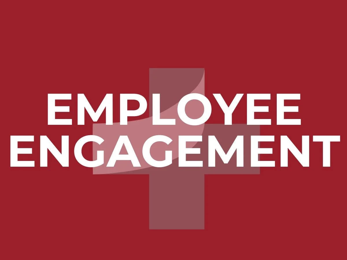 Graphic displaying the phrase ‘Employee Engagement’ in bold white text on a maroon background with a translucent plus-sign shape behind it, representing motivation, connection, and alignment.