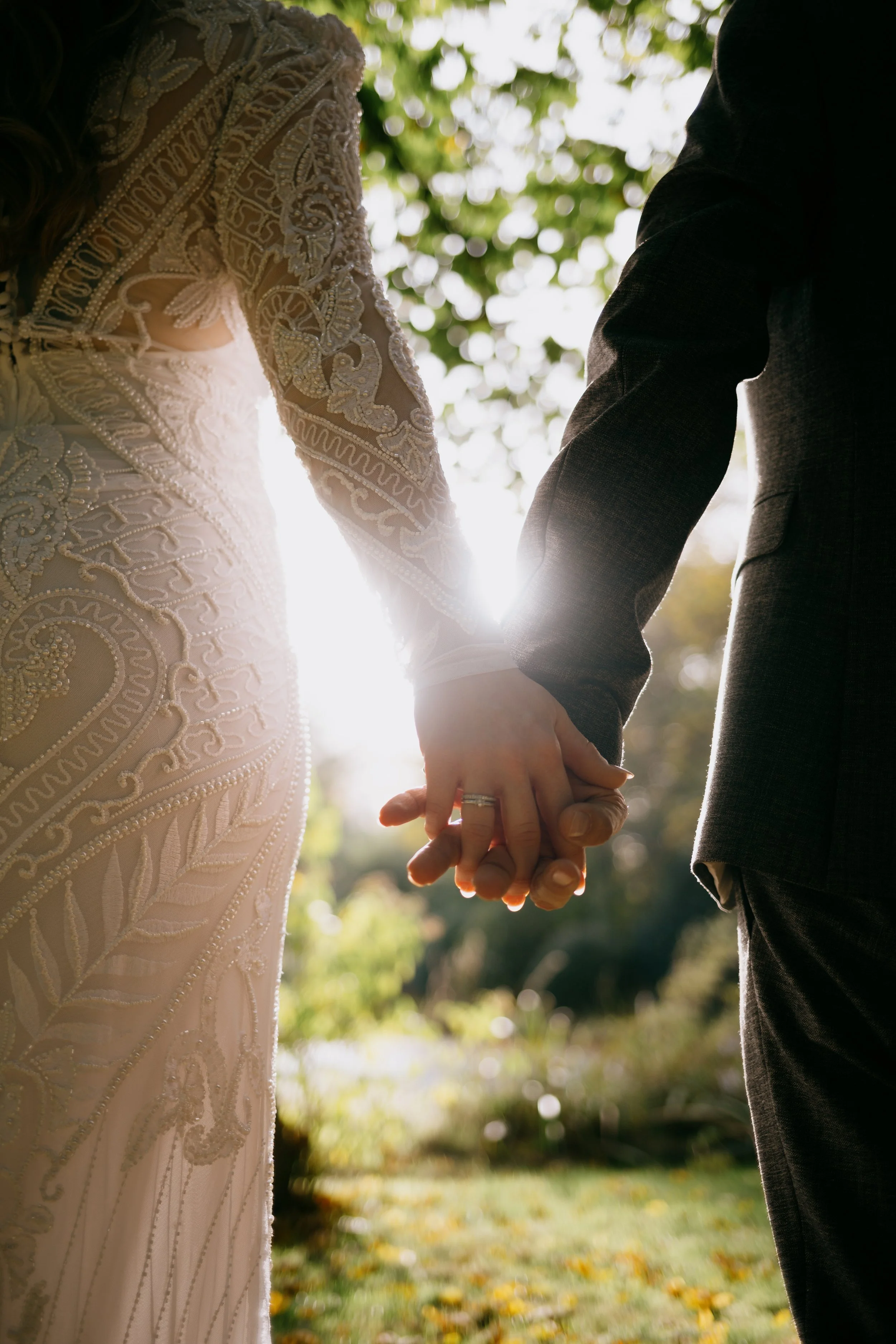 Nahaufnahme eines verheirateten Paares, das sich an den Händen hält, mit Fokus auf das Brautkleid und den Ehering.