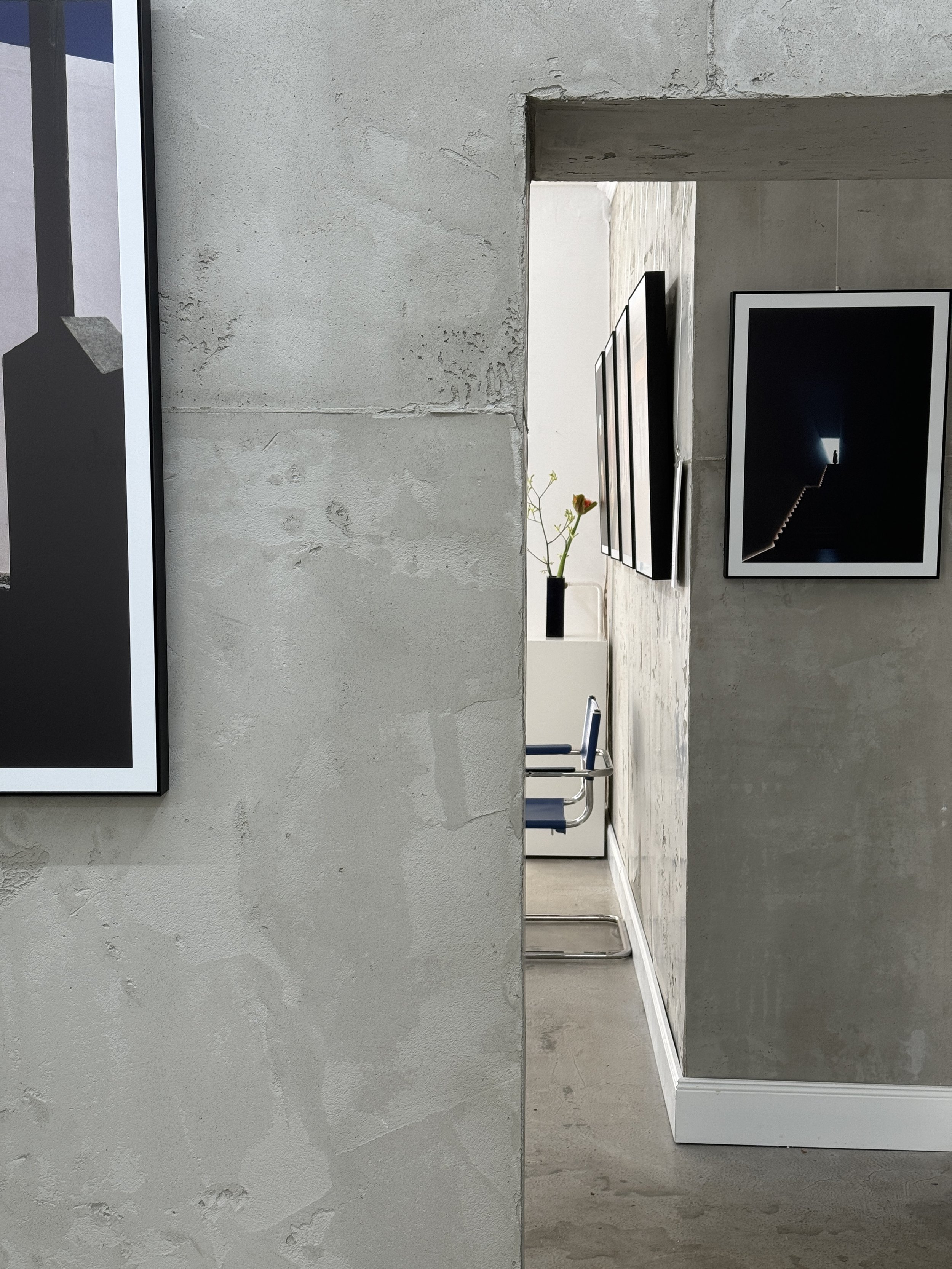 Ein Blick in einen modernen, minimalistischen Ausstellungsraum mit Fernsehern an der Wand und einem Tisch mit Stühlen im Hintergrund.