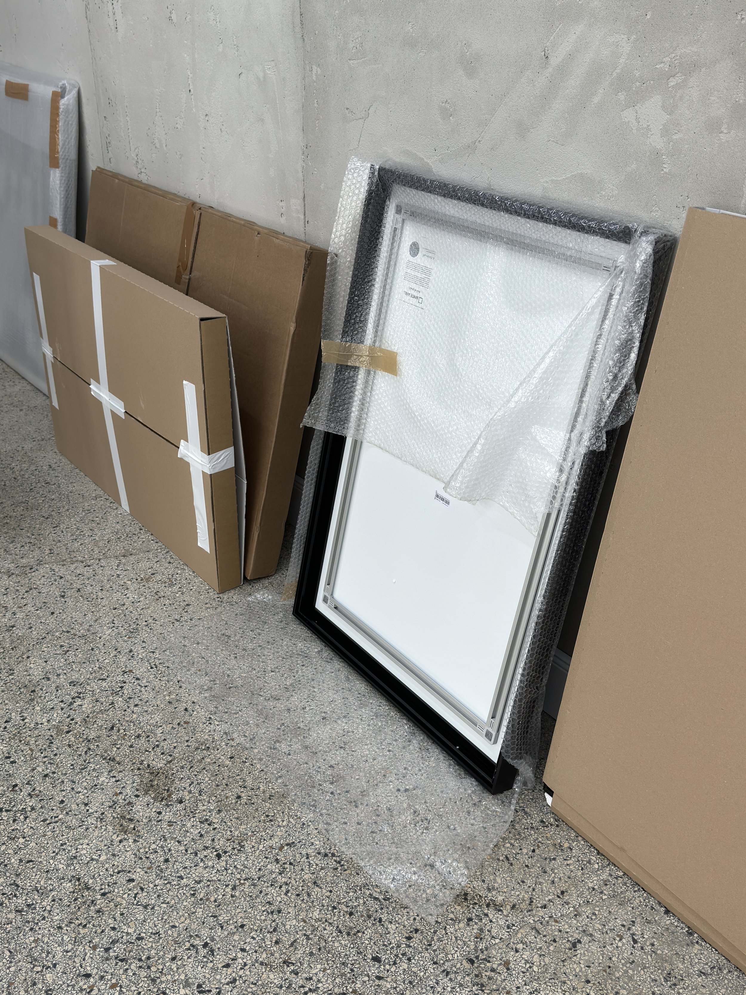 Verpackte Fenster und Kartons gegen eine Betonwand in einem Raum.