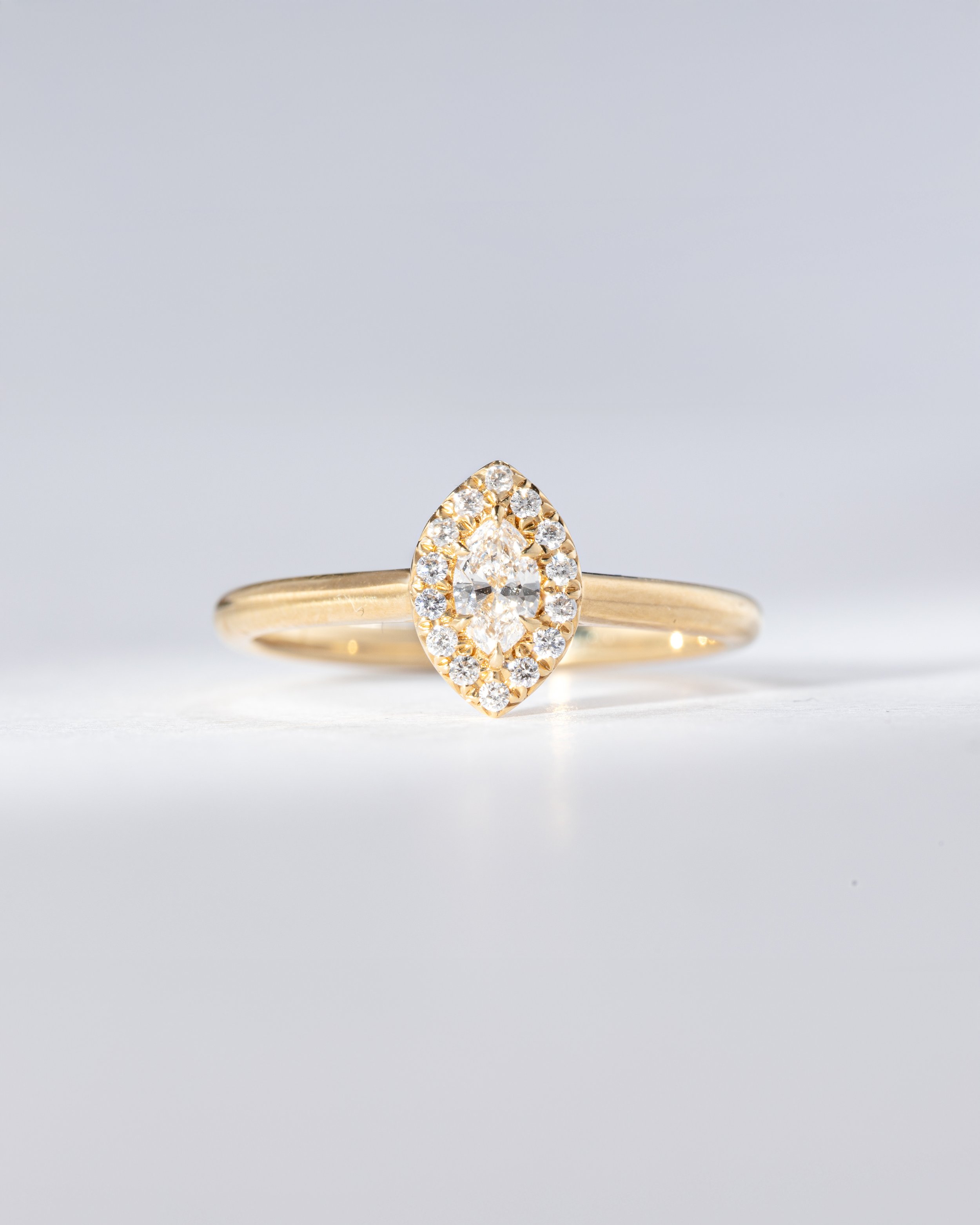 Goldring mit einem ovalen Diamanten in der Mitte, umgeben von kleineren Diamanten, auf hellem Hintergrund.