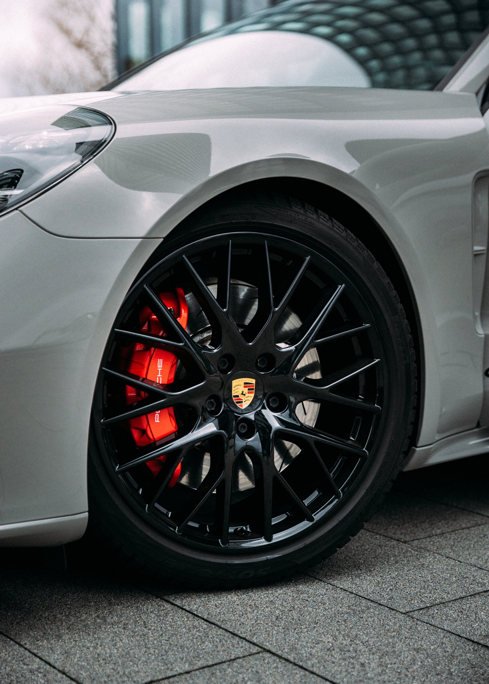 Nahaufnahme eines weißen Porsche Sportwagens mit schwarzen Felgen und roten Bremsen, die Porsche-Logo sind sichtbar.