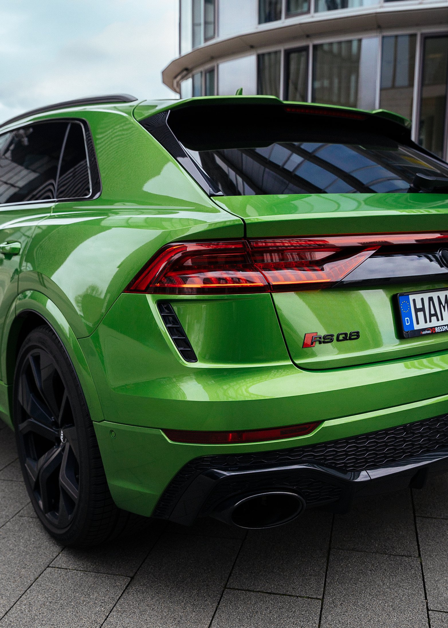 Grüner Audi RS Q8 Sportwagen von hinten, vor moderner Glasfassade