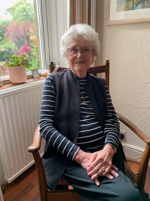 Photo of Rita Crombie sitting in a chair by a window