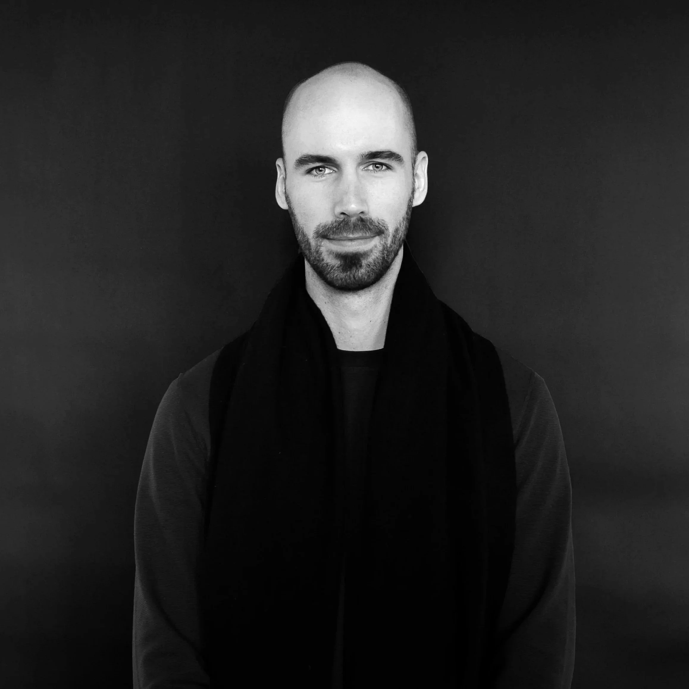 A man with a shaved head and beard holding a microphone, wearing headphones and a conference badge, speaking at an event.