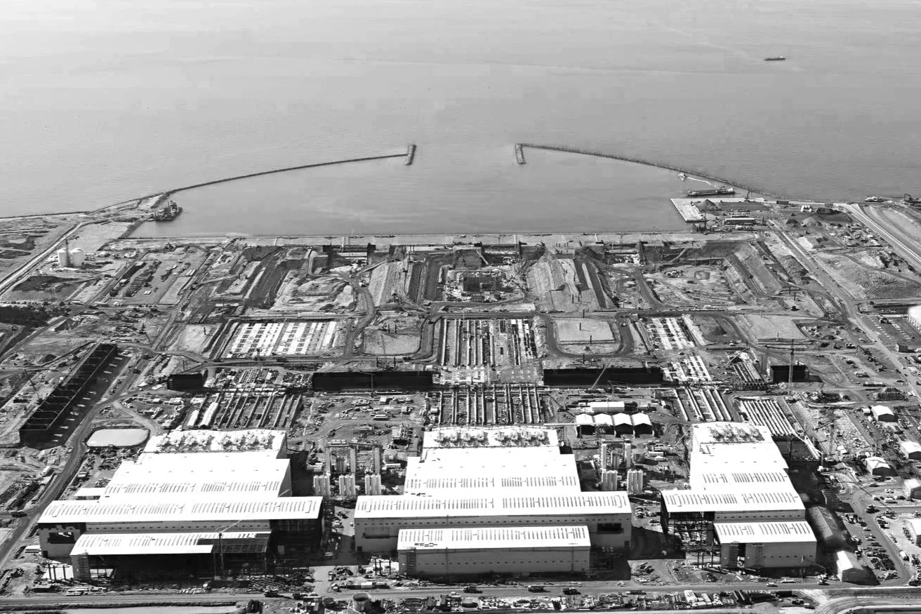 Construction workers working inside a large building with steel framework and cranes.