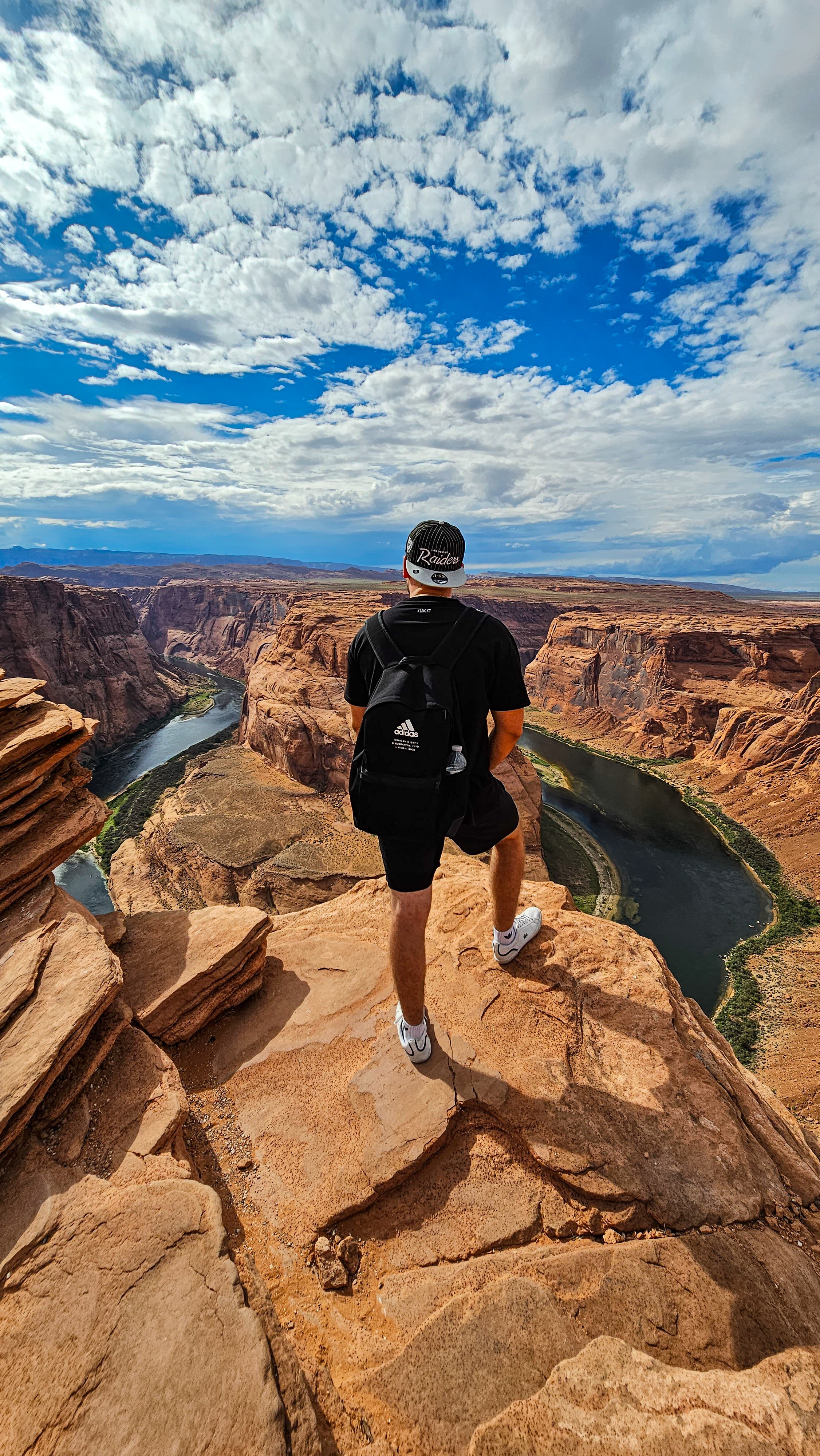 Ein Mann steht auf einem Felsen und blickt auf den Colorado River in der Antelope Canyon, umgeben von roten Sandsteinwänden und einem bewölkten Himmel.