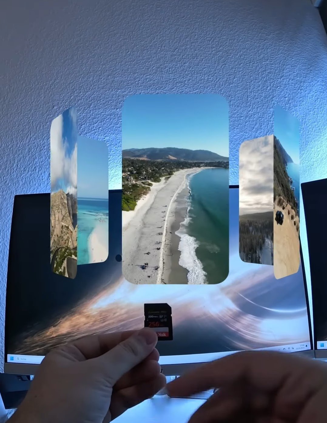 Person hält eine Speicherkarte vor einem Bildschirm mit digitalem 3D-Display, das fünf wechselnde Strand- und Küstenbilder zeigt.