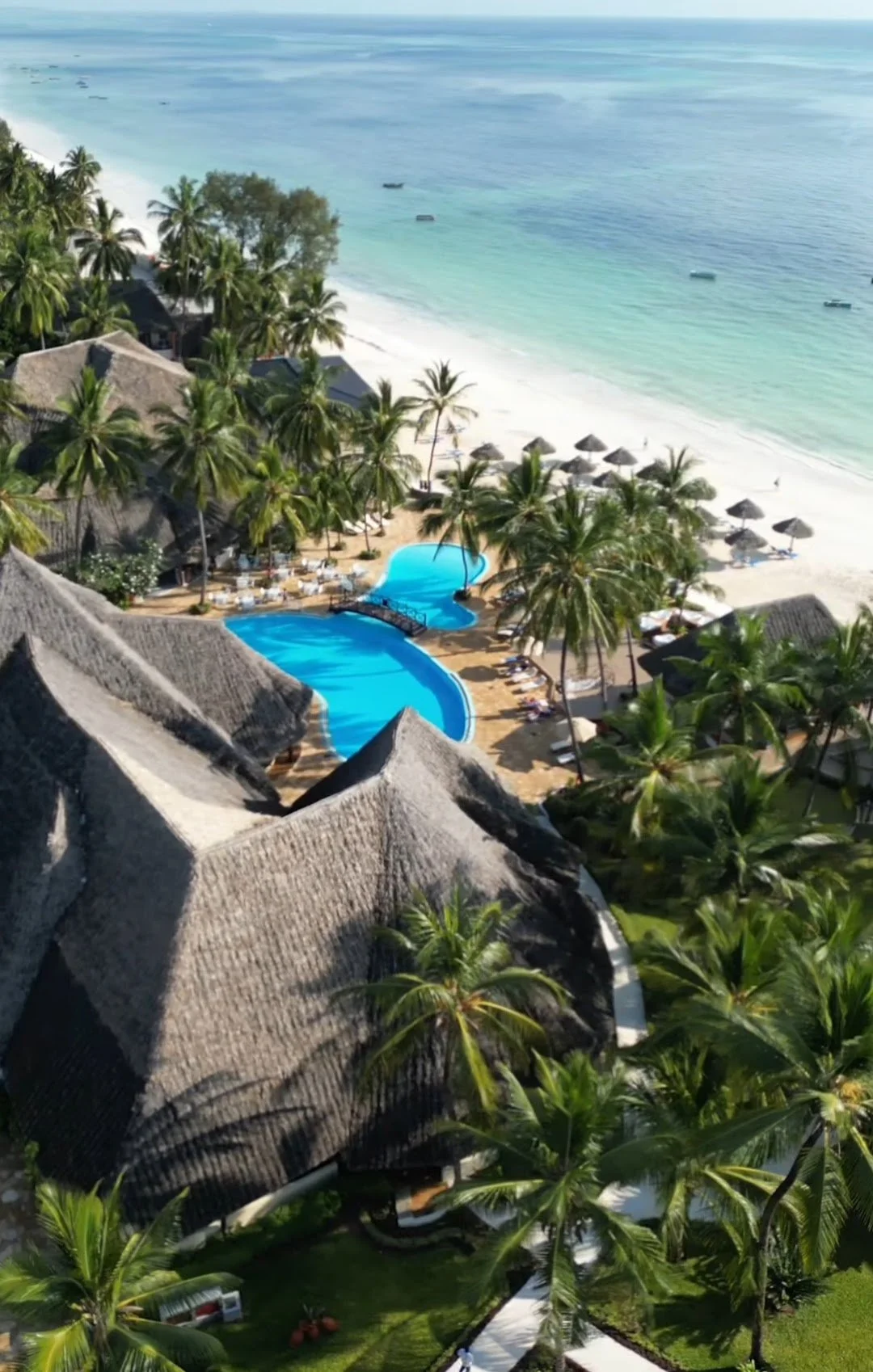 Strandhotel mit Pool umgeben von Palmen auf einer tropischen Insel.