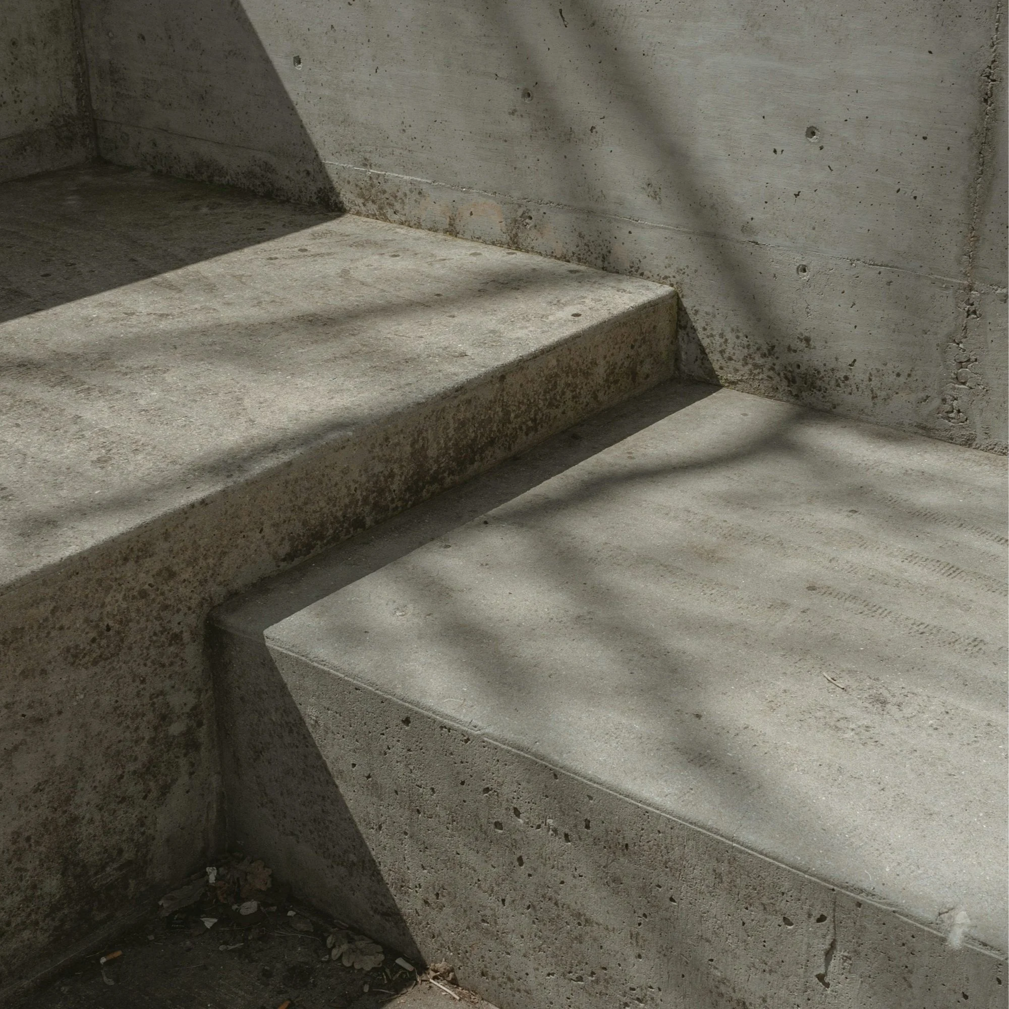 Concrete stairs casting shadows on the ground with a concrete wall in the background.
