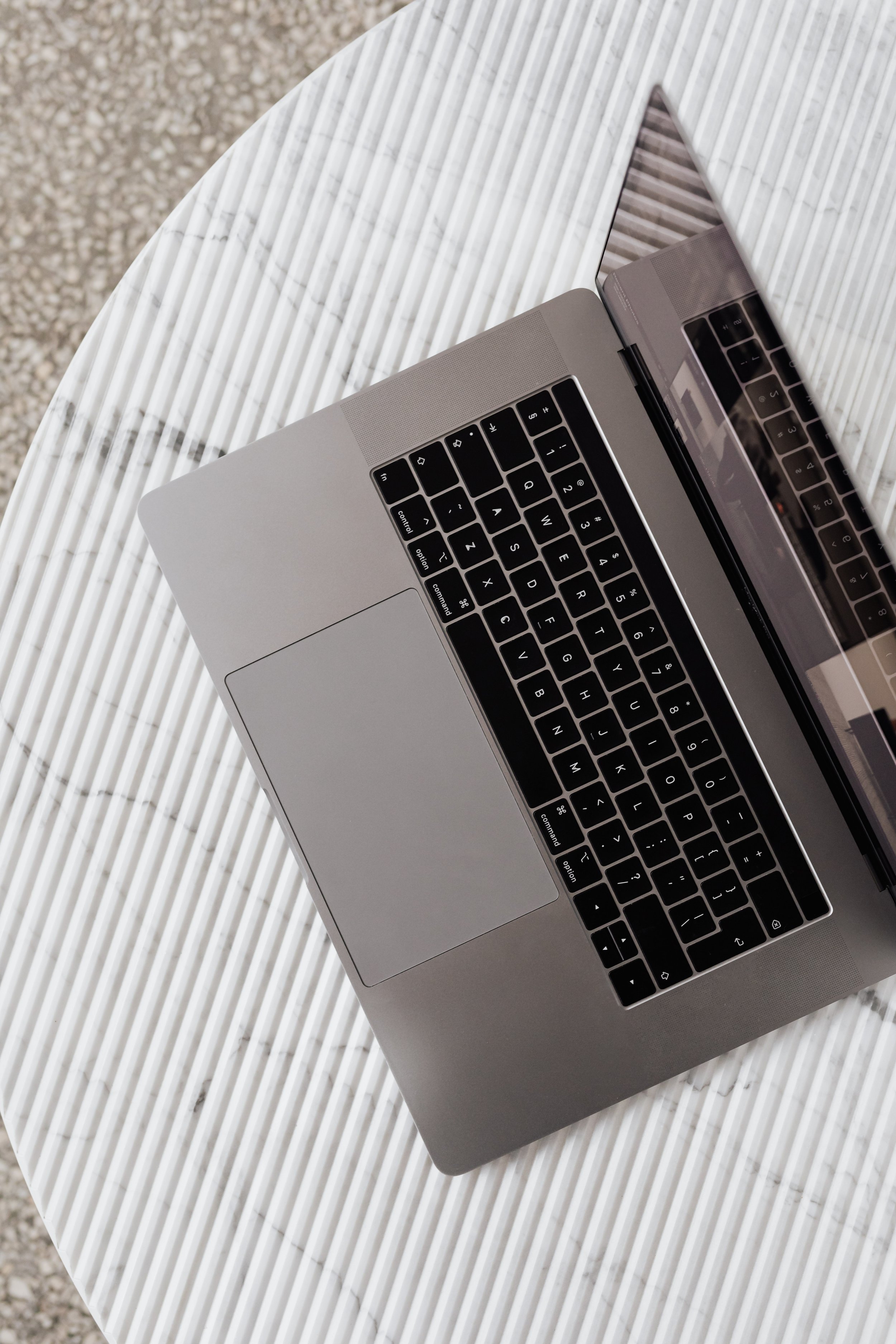 A silver laptop with a black keyboard resting on a white, round, textured table.