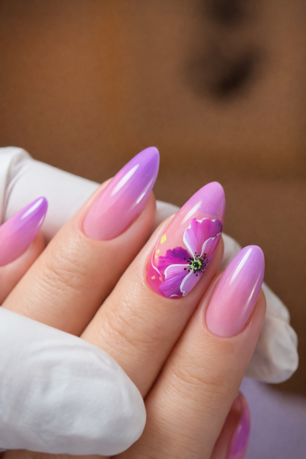 Uña decorada con esmalte rosado y diseño de flor rosa y blanca con puntos verdes y detalles negros.