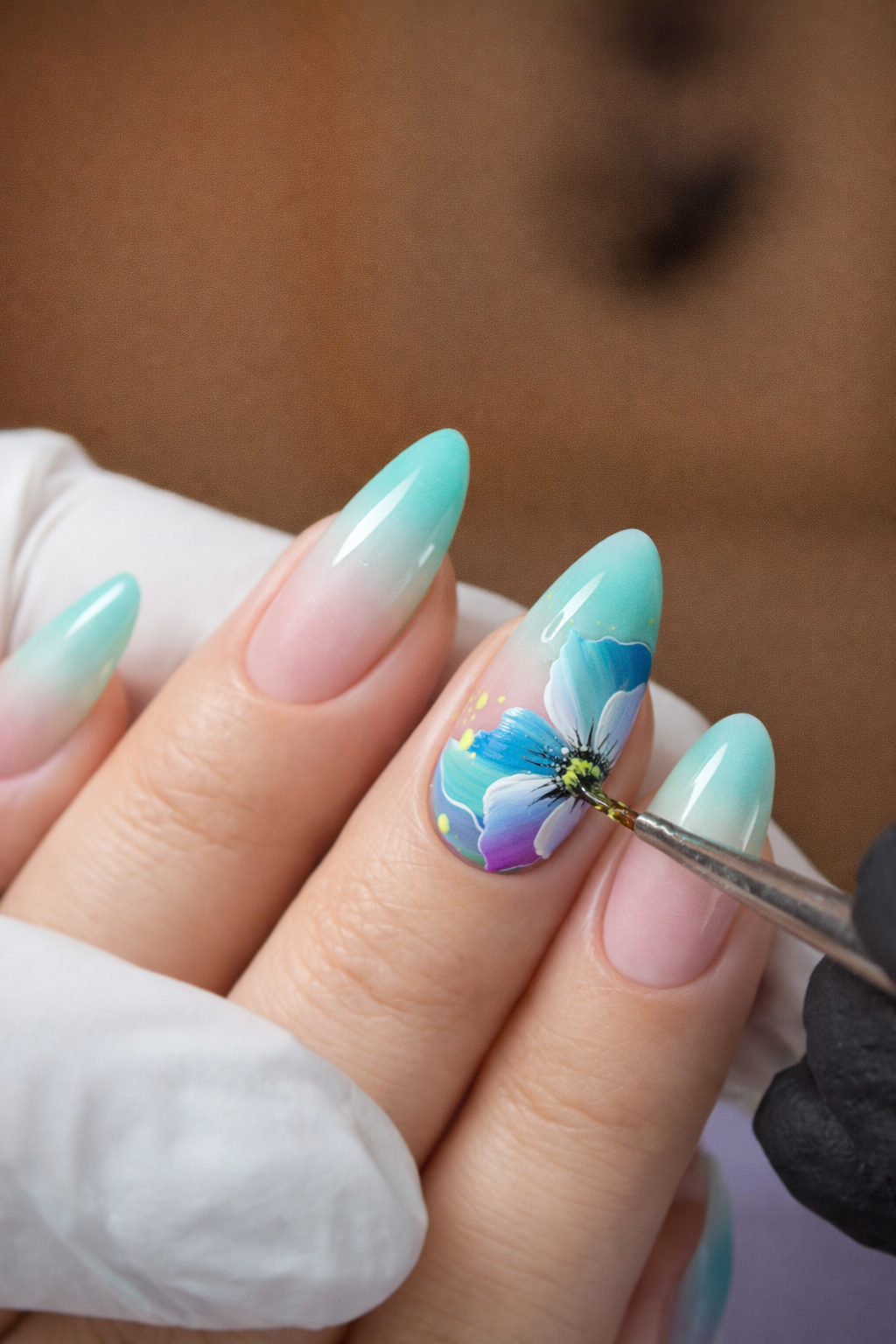 Manicura con esmalte en tonos de azul y verde y una uña decorada con pintura de una flor de colores vibrantes.